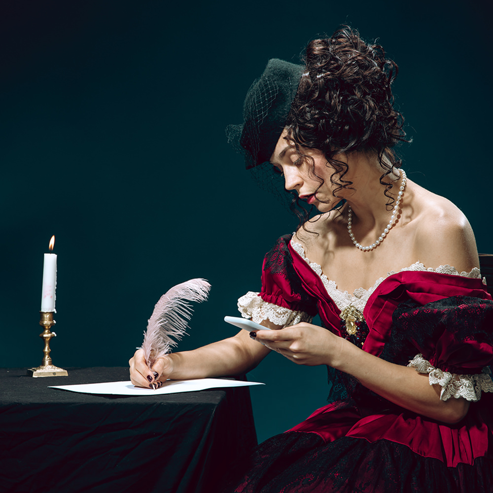 Frau im roten Kleid schreibt auf Papier mit einer Feder. In einer Hand hält sie ein Smartphone.