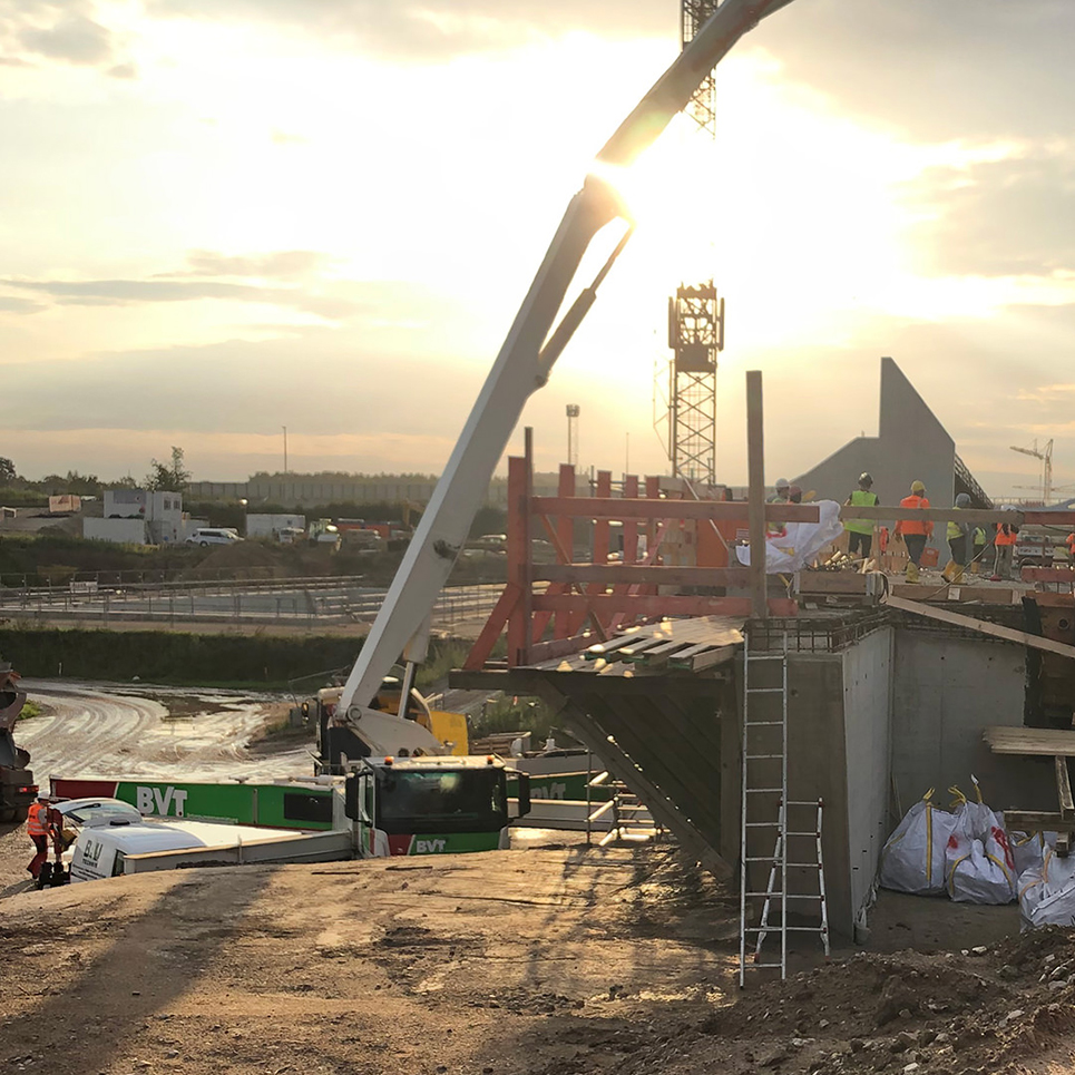 Bau der Autobahnbrücke über die A3 bei Sonnenaufgang mit Bauarbeitern und Kränen.